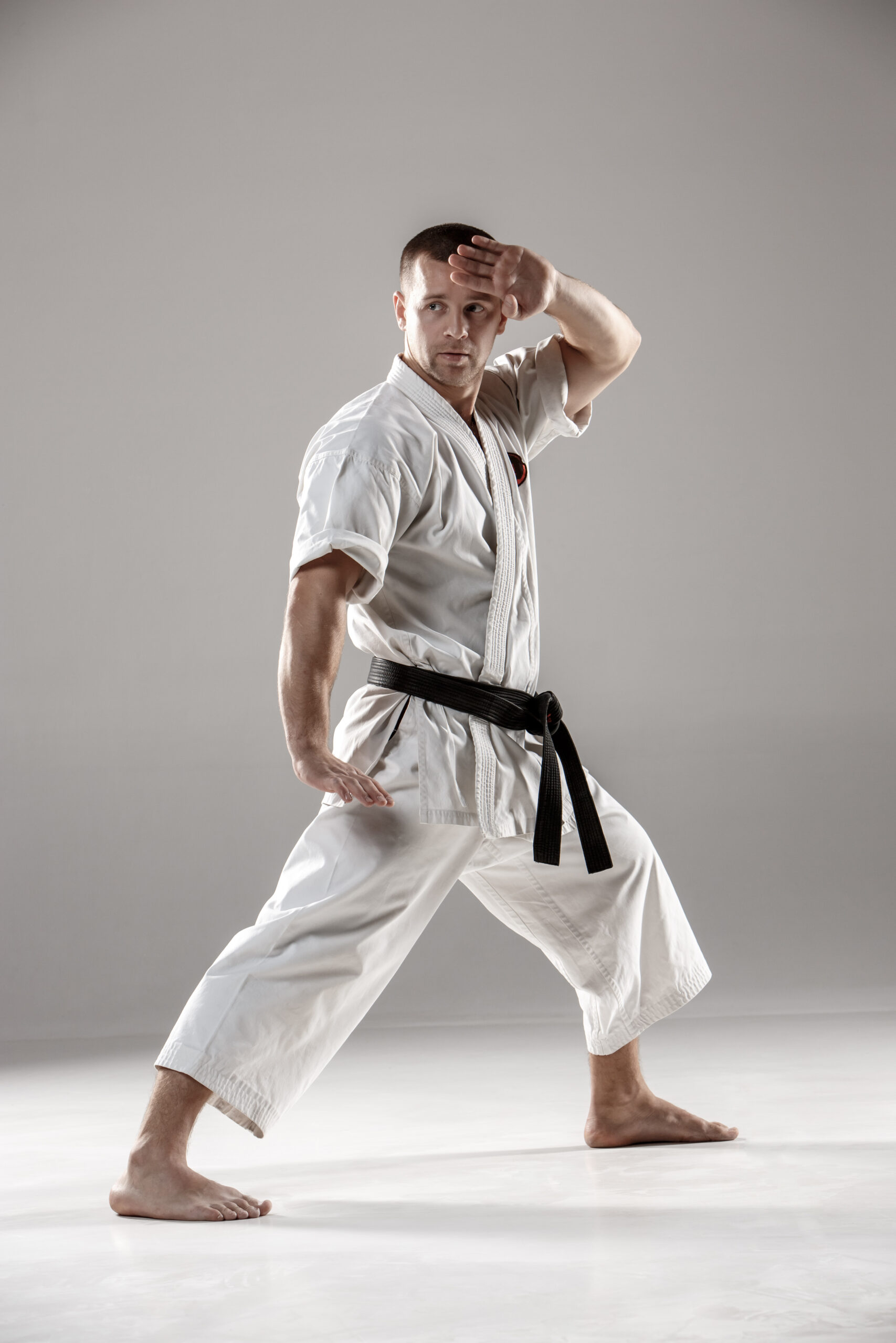 Man in white kimono and black belt training karate over gray background.